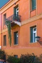 Orange stucco building with deep green and white casement windows in Athens Greece with wrought iron balcony and succulent growing