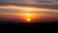 Orange sun setting behind dark silhouetted hills with dramatic clouds in the sky 555 Royalty Free Stock Photo