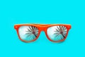 Orange sunglasses with palm tree reflections isolated in intense cyan blue background. Minimal image concept for ready for summer