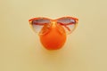 Orange in sunglasses on pastel yellow paper, trendy flat lay. su