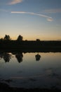 An orange sunset against a blue sky with cirrus white clouds reflecting in the the lake and reflections on the water Royalty Free Stock Photo