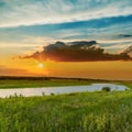 orange sunset in clouds over river in green grass Royalty Free Stock Photo