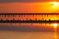 Orange sunset, dramatic and majestic sky over beach with sun reflection in water. Wood posts for salt extraction of Royalty Free Stock Photo