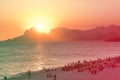 Orange sunset by the ocean in Piratininga, Niteri, with sun dipping behing the Gavea Stone in Rio de Janeiro. A beach full of peop