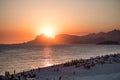 Orange sunset by the ocean in Piratininga, Niteroi, with sun dipping behing the Gavea Stone in Rio de Janeiro. A beach full of peo
