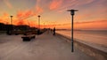 Orange  sunset pink sky dramatic clouds on promenade seaside street lamp lantern people walk on front seagull fly nature landscape Royalty Free Stock Photo