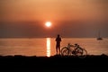 Orange sunset at promenade woman with bike relaxing and watching pink cloudy evening sky sun down gold hour at sea nature landsc