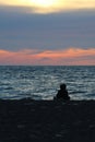 Orange sunset on the sea, the silhouette of a man on the background of the sunset. A girl sits on the beach at sunset