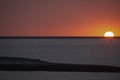 Orange sunset - Sun on horizon partly refracted deep orange and black river sand foreground clean Royalty Free Stock Photo