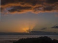 Orange sunset with sun rays, sea and clouds view. The sun sets in the atlantic ocean seen from above over green bushes Royalty Free Stock Photo