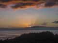 Orange sunset with sun rays, sea and clouds view. The sun sets in the atlantic ocean seen from above over green bushes Royalty Free Stock Photo