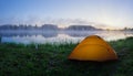 Orange tent on green grass of foggy lake at sunrise Royalty Free Stock Photo