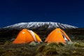 Orange tents illuminated before Mount Kilimanjaro during night