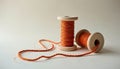Orange thread unwinds from wooden spool on light surface. One spool stands upright, full of vibrant yarn. Another lies down, long Royalty Free Stock Photo
