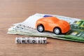 Orange toy car on few 100 euro banknotes and credit word. Concept of car buying, renting, service, repair and insurance costs. Royalty Free Stock Photo