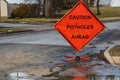 Orange triangular road sign on a small suburban street that says caution potholes ahead.