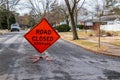 Orange triangular road sign on a small suburban street that says Road Closed Potholes. Royalty Free Stock Photo