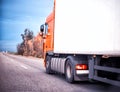 An orange truck is transporting goods in a refrigerated trailer on a motorway. Logistics and industry concept in cargo