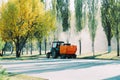 Orange vacuum sweeper towed by a blue tractor removes dust and debris from the roads : September 20, 2021 Agidel, Russia