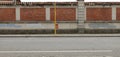 Orange waste bin hanged on yellow pole on concrete sidewalk. Brick and cement wall with erased graffiti on behind, street in front Royalty Free Stock Photo