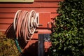 Orange water hose on winding holder attached to side of orange - red building with flowr beds - Close-up