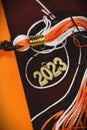 Orange, white, and brown graduation tassel and gold 2023 charm laying on seat