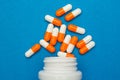 Orange white capsules pills were poured from a white bottle on a blue background. Medical background, template. Royalty Free Stock Photo