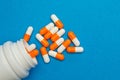 Orange white capsules pills were poured from a white bottle on a blue background. Medical background, template. Royalty Free Stock Photo