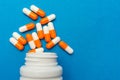 Orange white capsules pills were poured from a white bottle on a blue background. Medical background, template Royalty Free Stock Photo