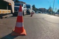 Orange, white traffic cone stands on road separating traffic flows, some lanes are completely filled with cars, others