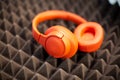 Orange wireless overhead monitor headphones lie on a dark foam rubber noise canceling panel. close-up soft focus, blur