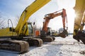 Orange and yellow powerful crawler excavators standing at a construction site against the backdrop of the sun