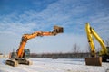 Orange and yellow powerful crawler excavators standing at a construction site on snowy ground on a sunny winter day