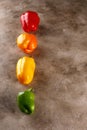 Orange yellow red green bell peppers over textured background. Overhead view of fresh organic vegetables on light wooden table. Royalty Free Stock Photo