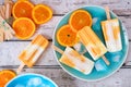 Orange yogurt popsicles on a blue plate, top view against white wood