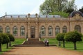 Exterior view of a historic Orangery lined by topiary trees