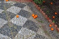 Oranges fallen from a tree on a diamond patterned pavement made from dark and light coloured pebbles