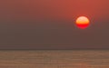 Reddish-orange sun glowing in darkening sky over ocean, sunset scenery