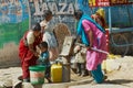 Women with kids pump water to plastic containers with a hand pump at the street in Orchha, India.
