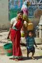 Young woman with a child carries plastic bucket with water at the street in Orchha, India.