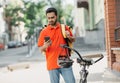 Order received. Guy in uniform with yellow backpack looks at smartphone, standing near a bicycle with helmet