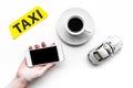 Order taxi online. Hand hold cell phone near taxi label, car toy on white background top view Royalty Free Stock Photo