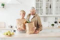 Ordering food online. Senior couple arriving from supermarket with grocery bag and unpacking in kitchen Royalty Free Stock Photo