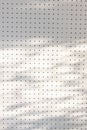 Orderly dot or holes rows and columns on white pegboard wall with shadow of leaves and branch tree