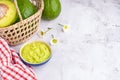 Organic avocado with seed, avocado halves in a basket, flowers, and fresh guacamole in a bowl and cloth on marble background. Top Royalty Free Stock Photo