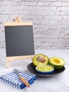 Organic avocado with seed, avocado halves, and fresh guacamole in a bowl on black plate with a small blackboard and cloth on Royalty Free Stock Photo