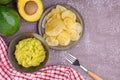 Organic avocado with seed, avocado halves, and fresh guacamole in a bowl with potato chips on a plate with cloth and cutlery on Royalty Free Stock Photo