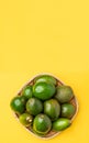 Organic avocados whole fruit in basket on yellow table background vertical top view.Healthy super foods for diet.Fresh vegetable