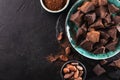 Organic broken chocolate in a vintage bowl, cocoa beans and cocoa powders on a dark textured background, top view, copy space.