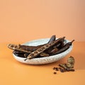 Organic carob pods, seeds in a ceramic plate on a beige background, locust bean healthy food, Ceratonia siliqua harnup. Natural Royalty Free Stock Photo